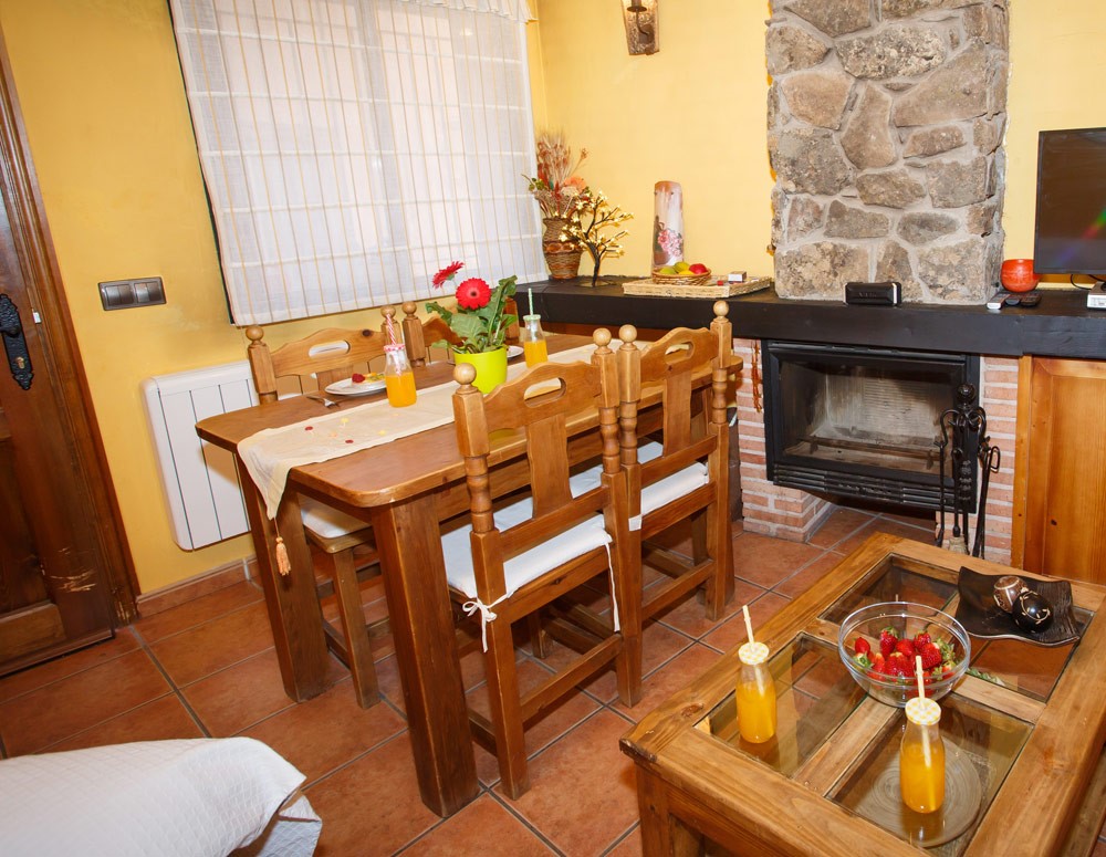 Salón con mesa con zumos de naranja, sillas de madera y chimenea