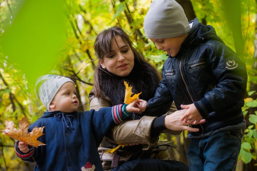 Madre con dos niños que intercambian hojas secas de árboles en el campo