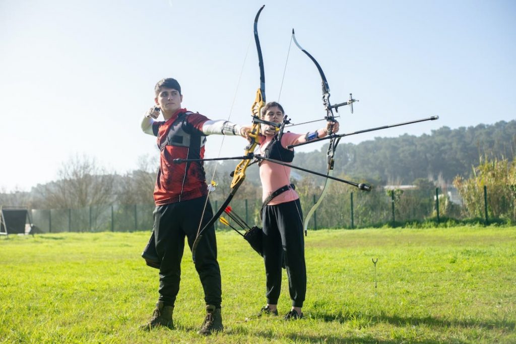 Chico y chica realiazando la actividad en la naturaleza de tiro con arco