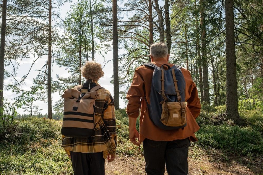 Pareja de ancianos caminando por bosque con mochilas en ruta de senderismo de la Sierra Norte de Madrid.