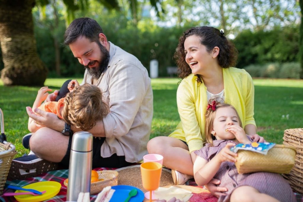 Padre, madre e hijos tumbados en pícnic al viajar en familia.